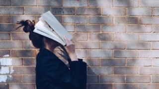 本で顔を隠す女性